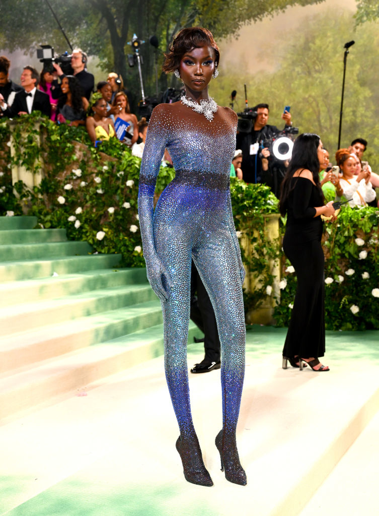 Person in a shimmering, full-body outfit poses on steps with spectators in the background