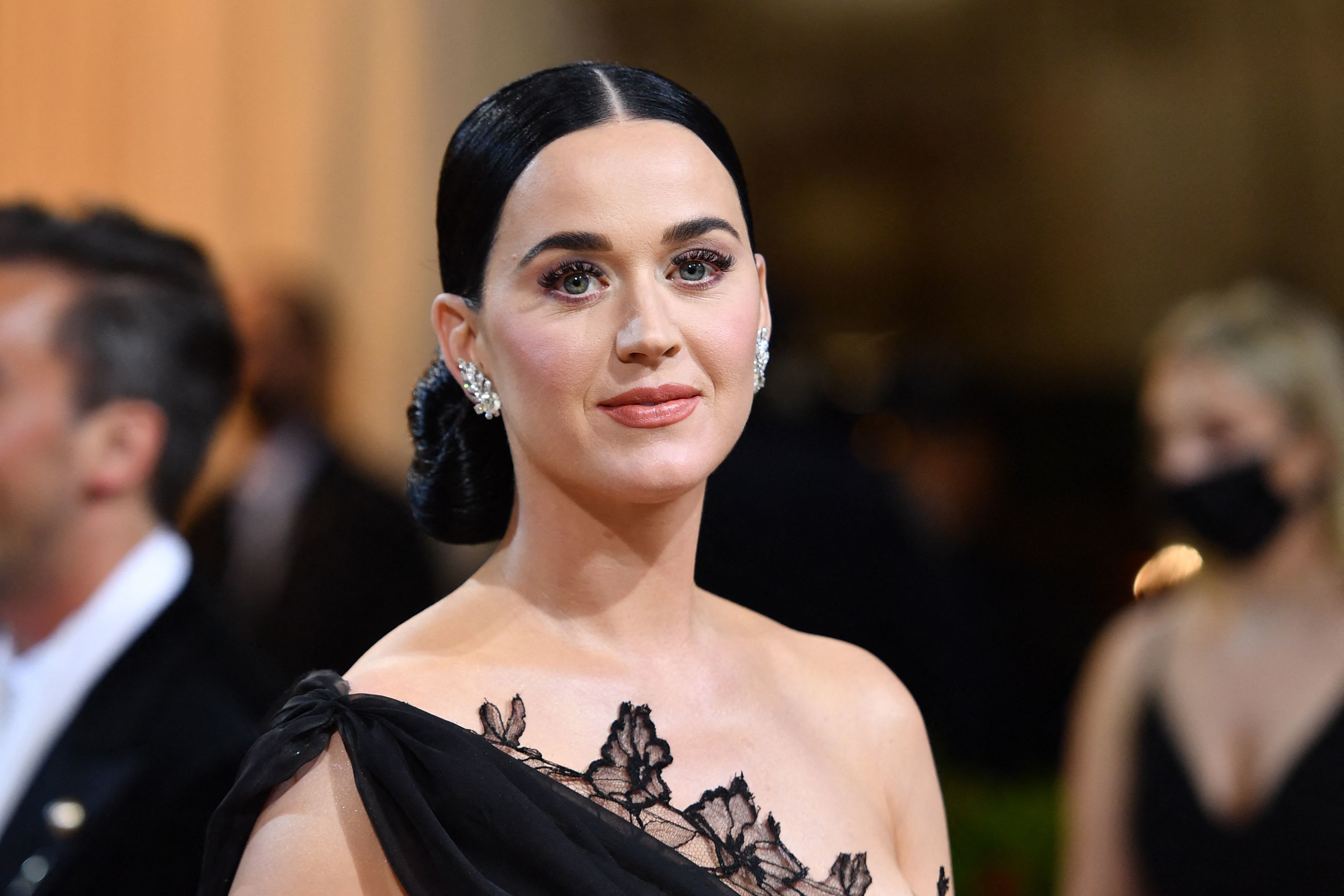 Katy Perry at an event, wearing an elegant off-shoulder gown with floral accents and statement earrings
