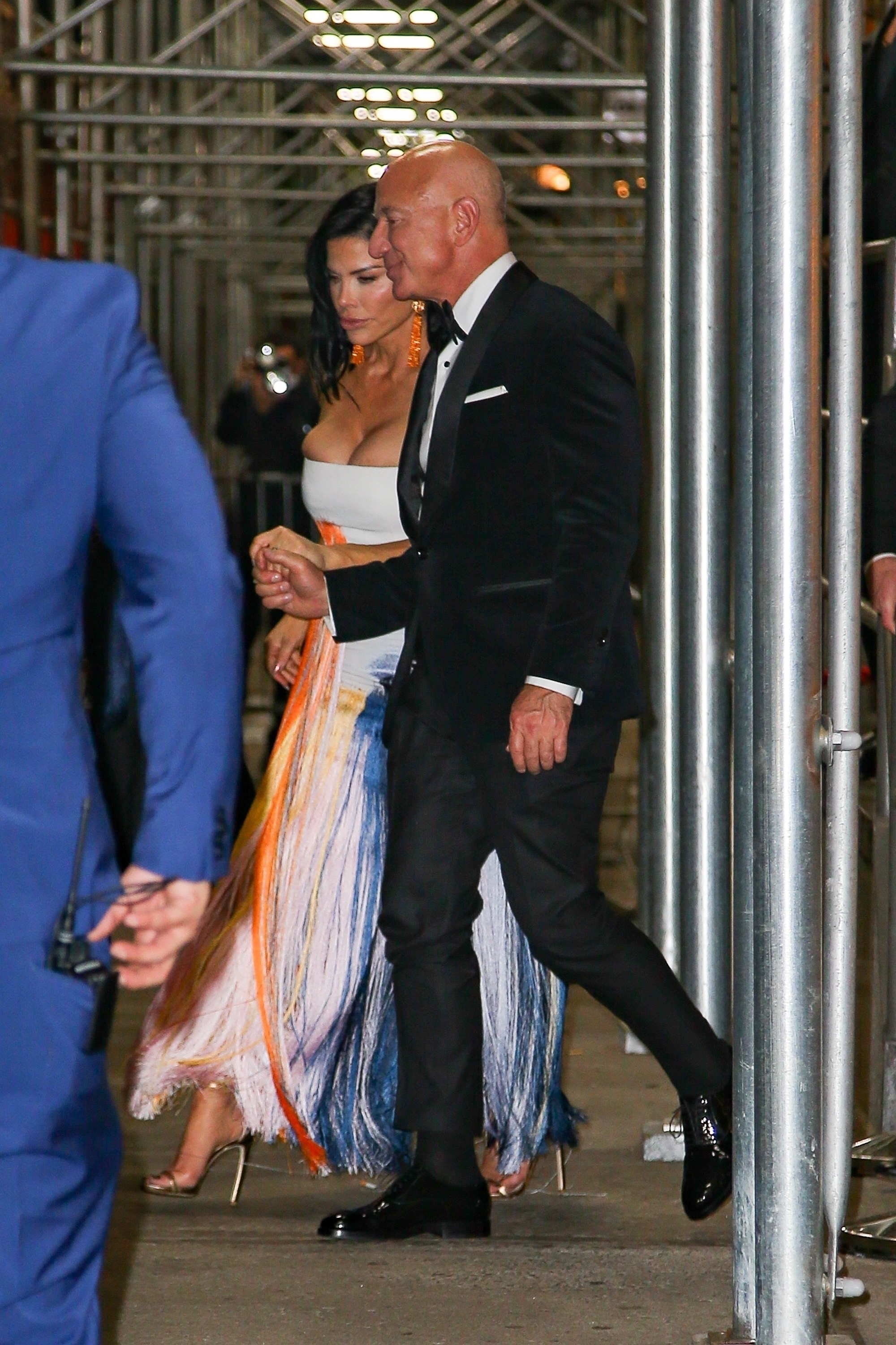 Two persons walking, woman in dress with layered fringe detail, man in black suit and bow tie