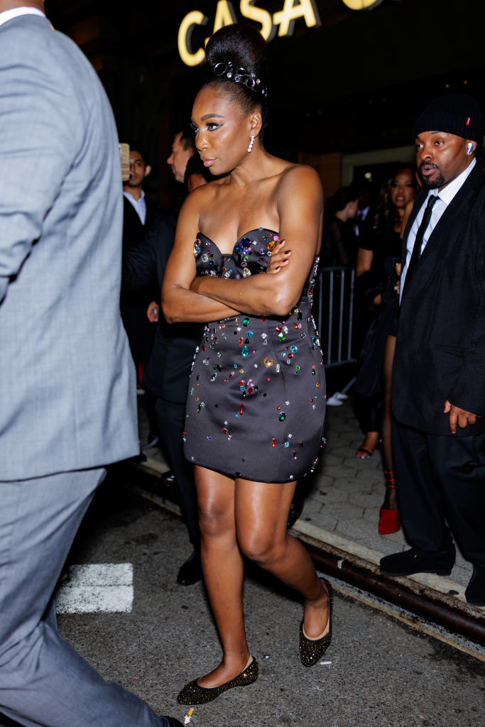 Woman in a strapless embellished dress with hair updo, standing on a street with onlookers