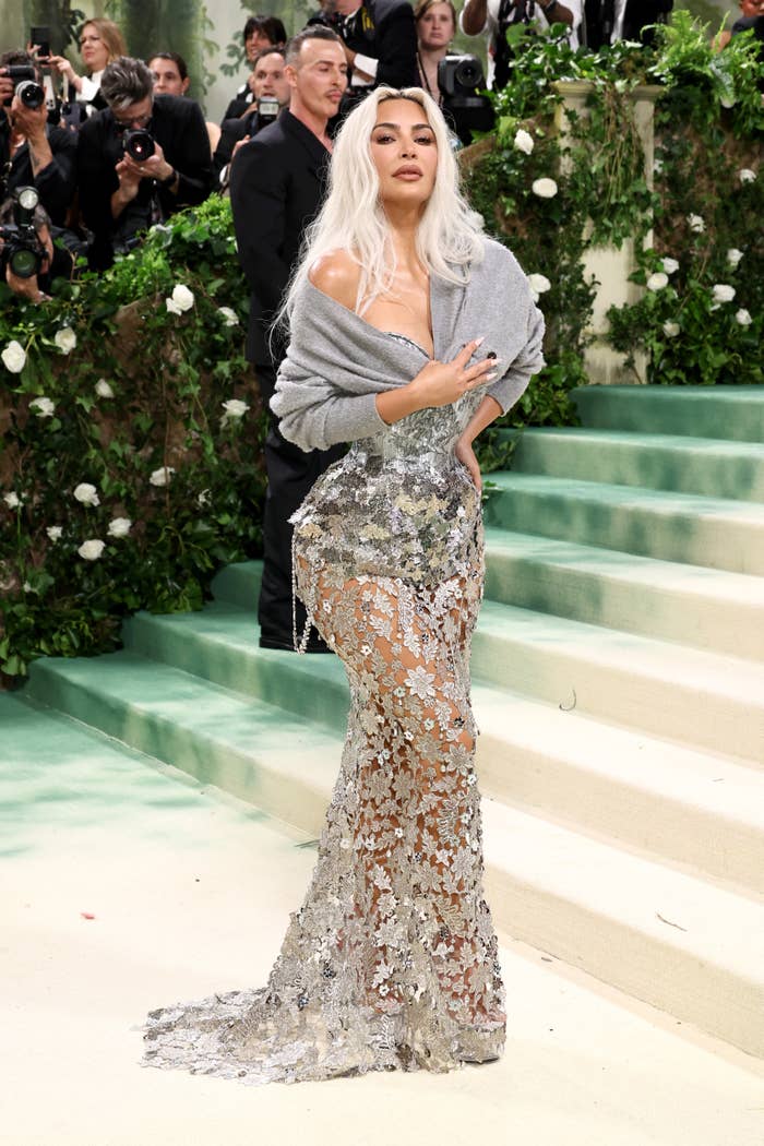 Kim Kardashian in a silver gown with floral accents, posing on Met Gala steps