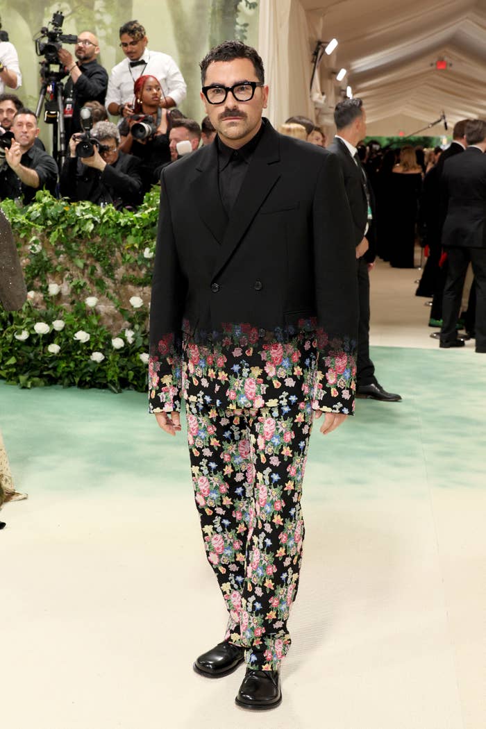 Dan Levy in a dark outfit with floral patterned pants and jacket at an event