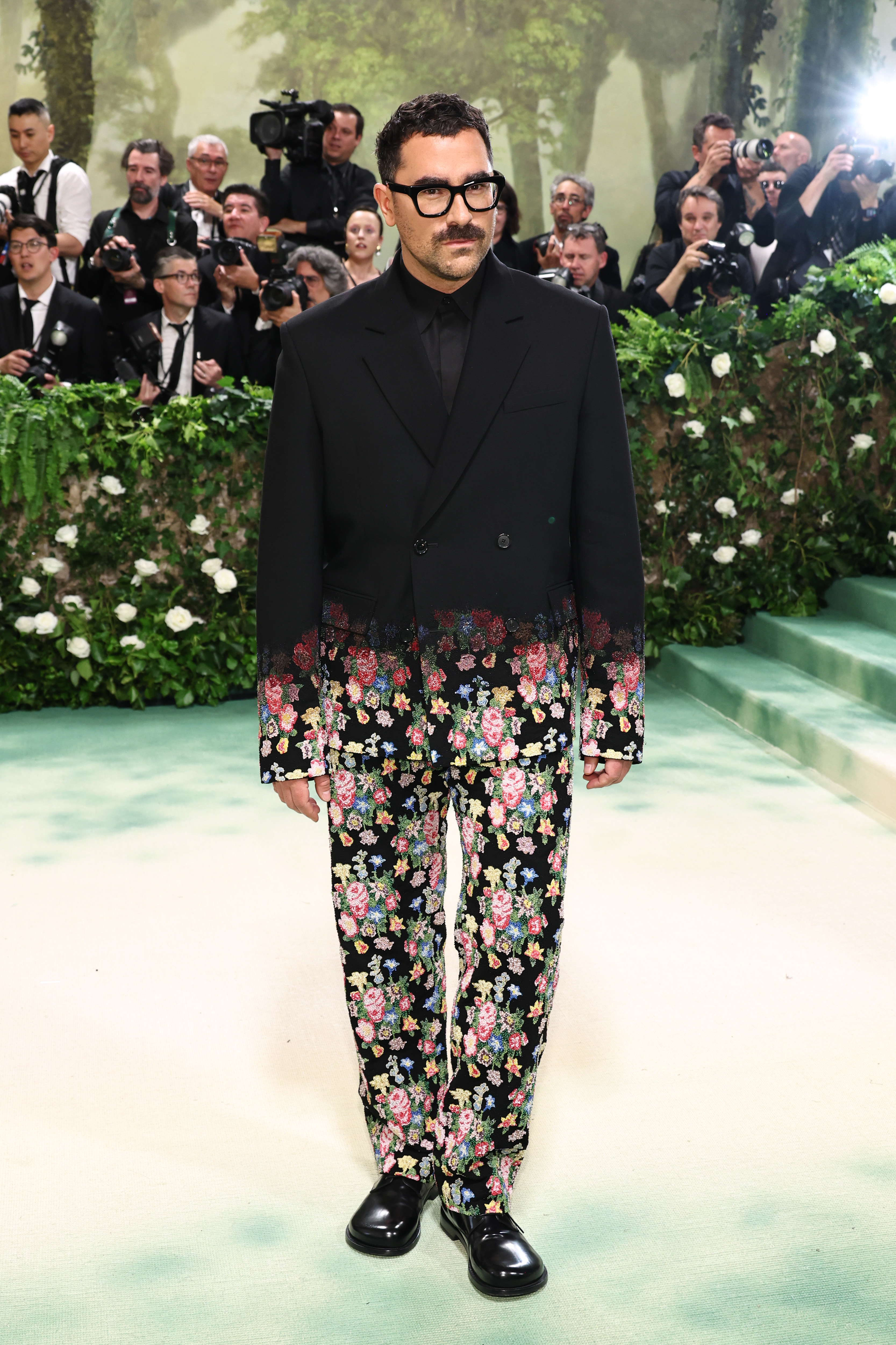 Dan Levy in floral suit at event with photographers in background