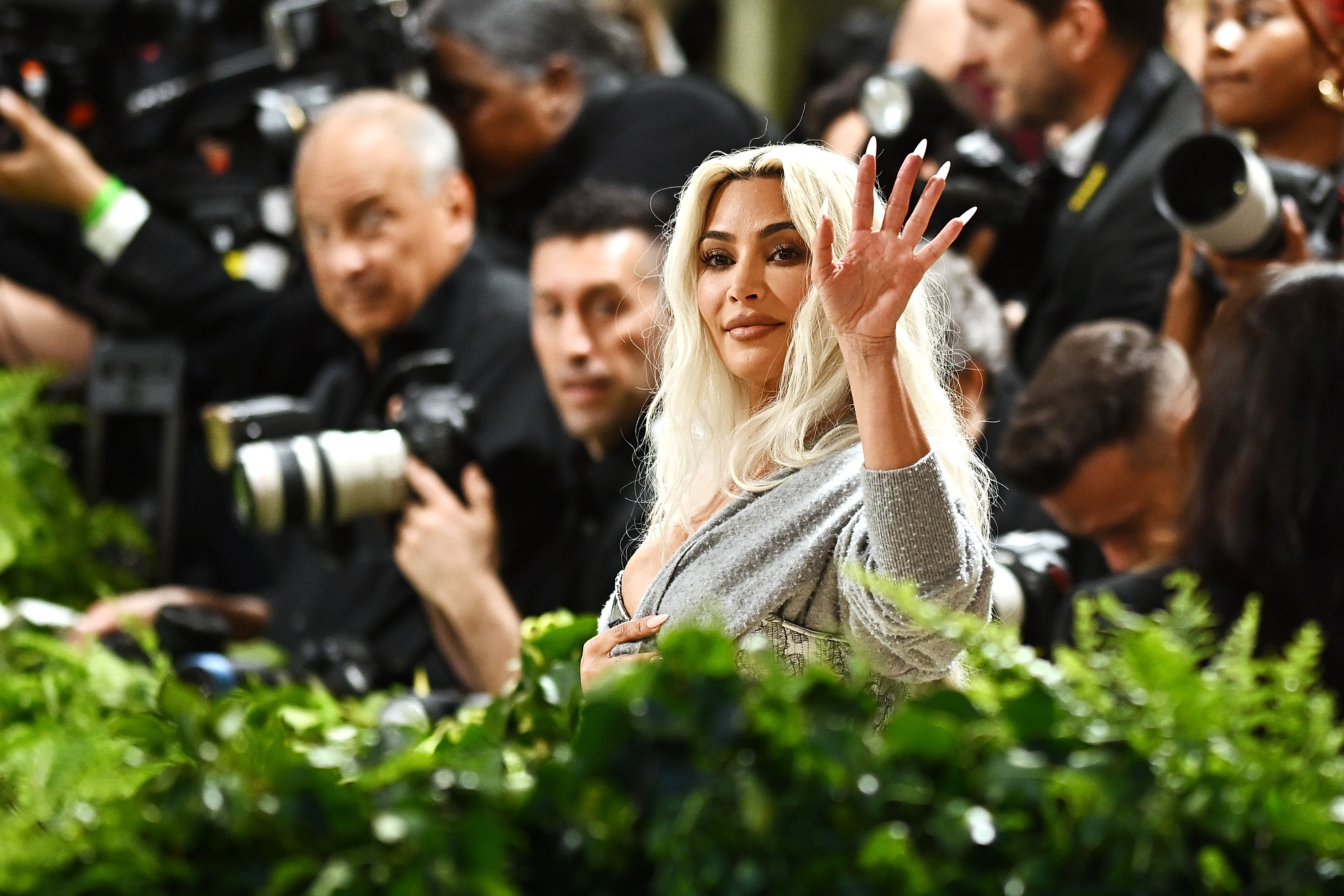 Kim Kardashian waving, surrounded by photographers at an event