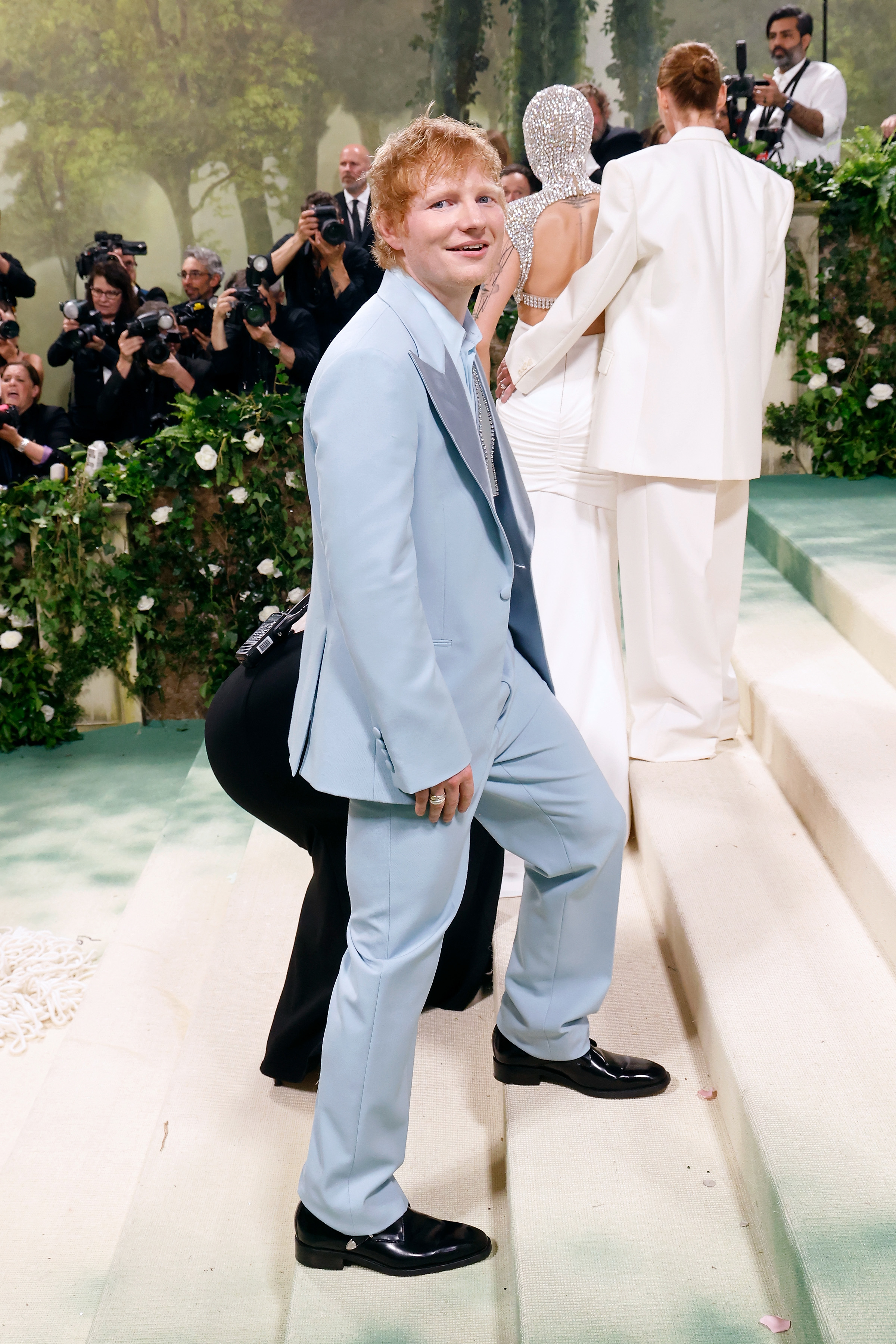 Ed Sheeran in a blue suit posing with photographers in the background at an event