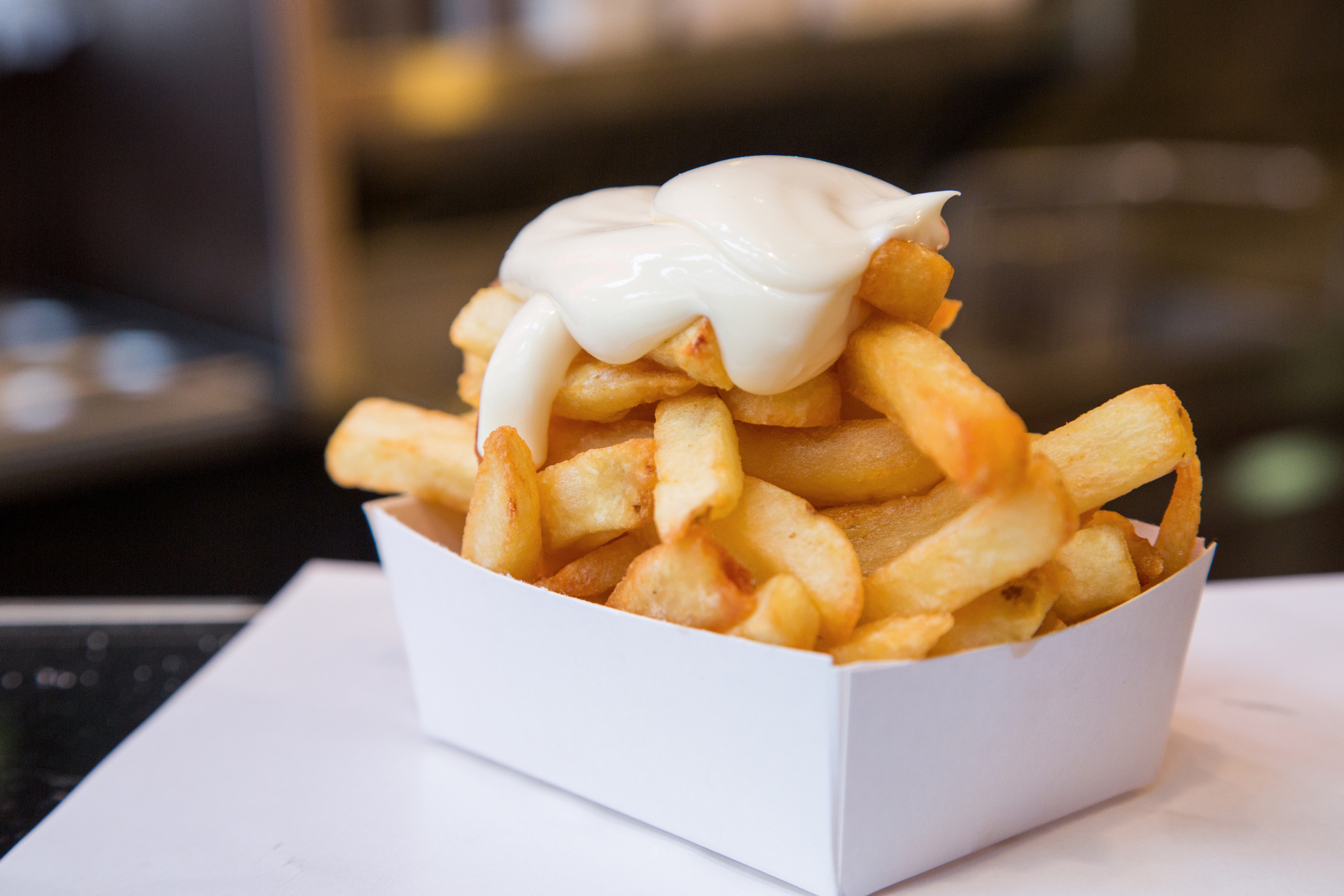 A portion of french fries in a container topped with a dollop of mayonnaise