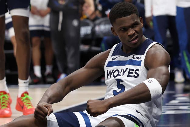 A basketball player in a Wolves uniform sits on the court appearing distressed during a game