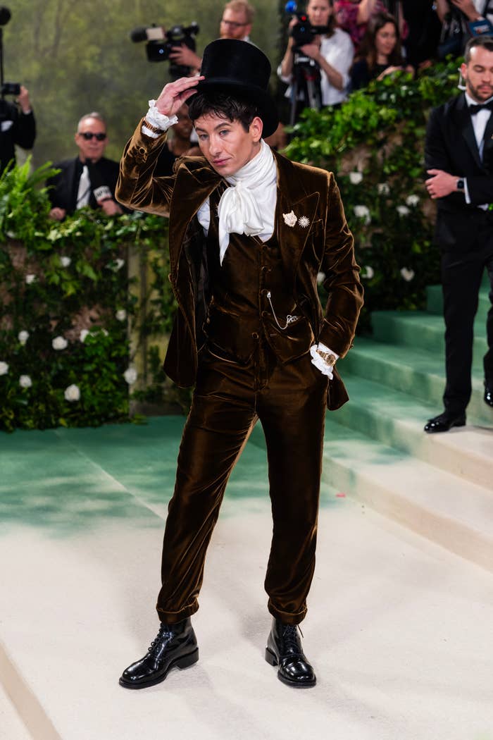 Ezra Miller posing in a velvet suit with sash and top hat at an event