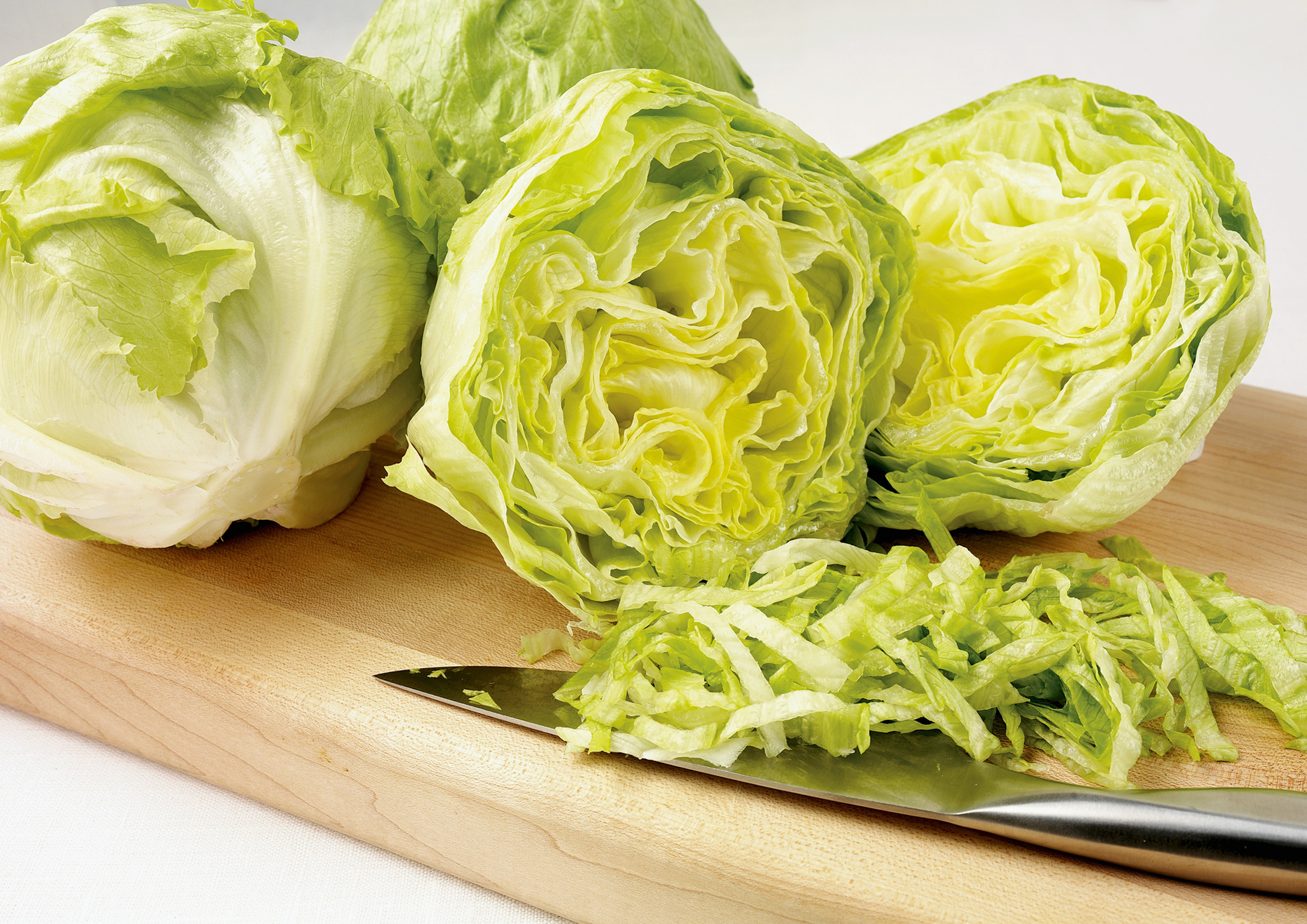 Head of iceberg lettuce cut in half on a board, with shredded pieces and a knife