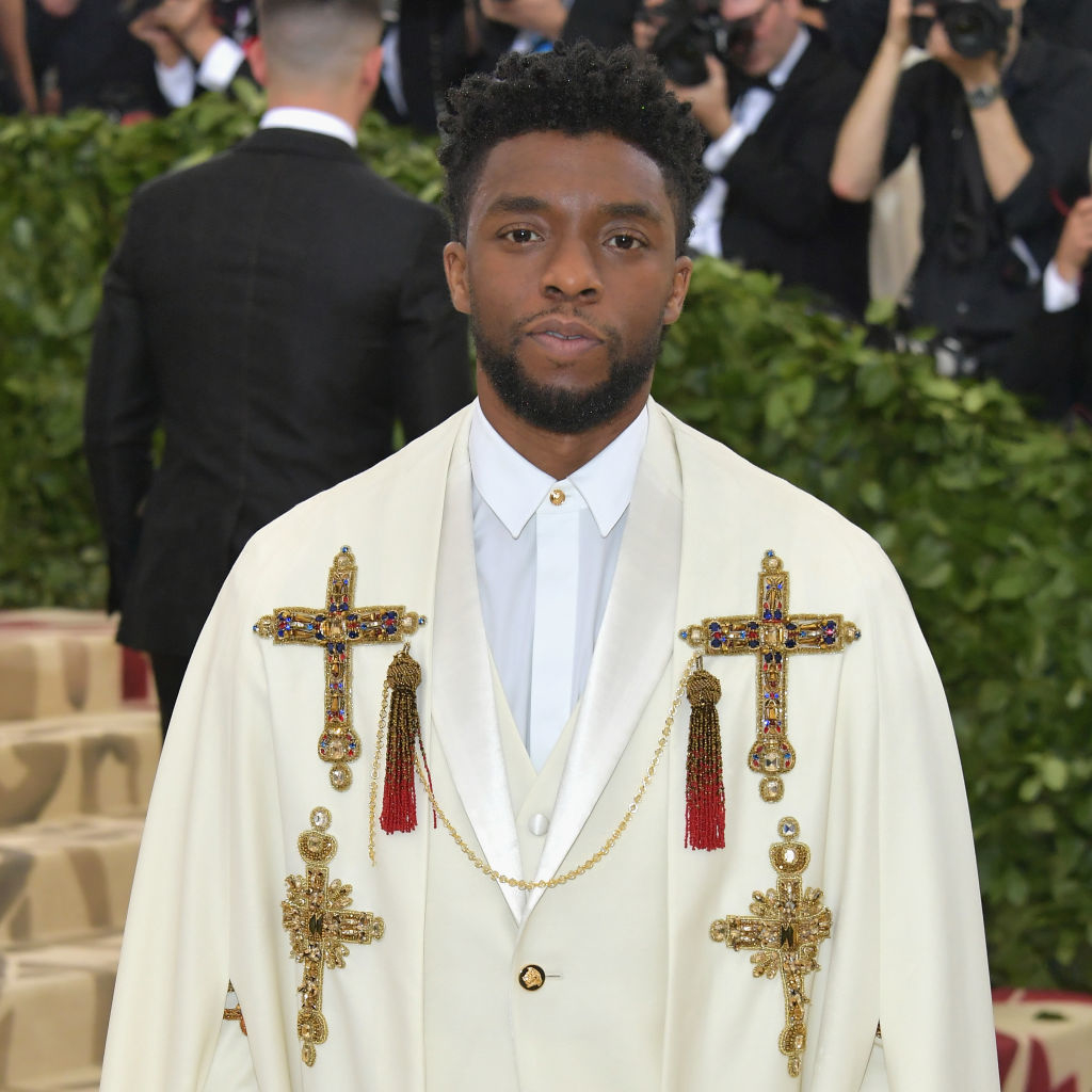 Chadwick Boseman in a white jacket with ornate gold crosses and tassels at a formal event