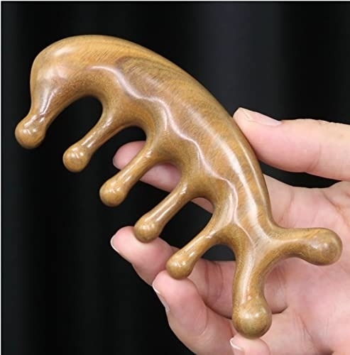 Hand holding a wooden scalp massage tool with four rounded prongs designed to fit fingers for grip