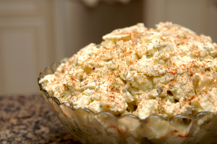 A close-up of a bowl of potato salad sprinkled with paprika, set on a countertop