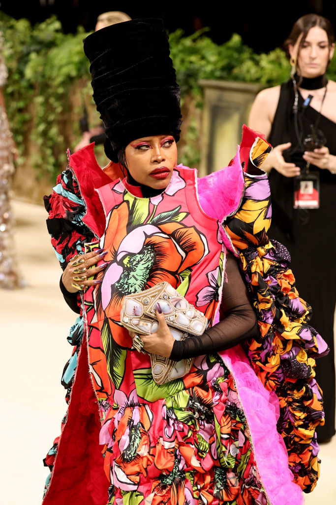 Erykah Badu at an event wearing a bold flower-patterned outfit and an exaggerated black headpiece