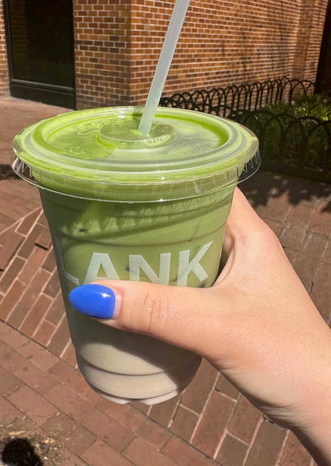 Hand holding a plastic cup of green smoothie with a clear straw