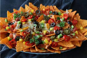A plate of nachos topped with melted cheese, jalapeños, olives, tomatoes, and herbs