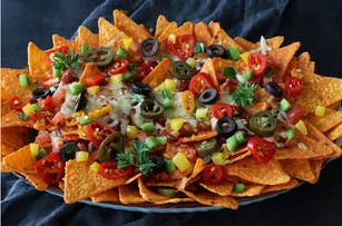 A plate of nachos topped with melted cheese, jalapeños, olives, tomatoes, and herbs