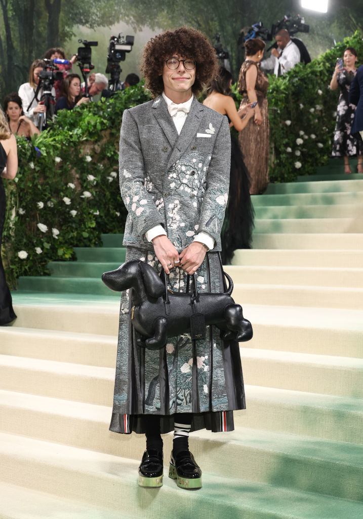 Reece in patterned suit with skirt and dog-shaped purse on the Met Gala's carpeted steps