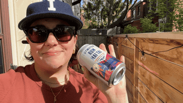Woman in sunglasses and cap holding a can of seltzer outdoors