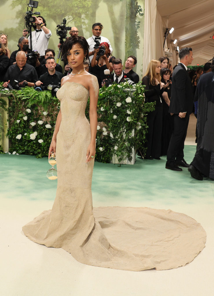Tyla in a strapless, floor-length sand gown with a train, posing on the red carpet with photographers in the background