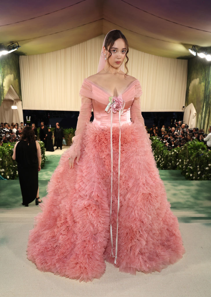 Laufey on a red carpet in an elaborate off-shoulder gown with ruffled skirt and a ribbon belt