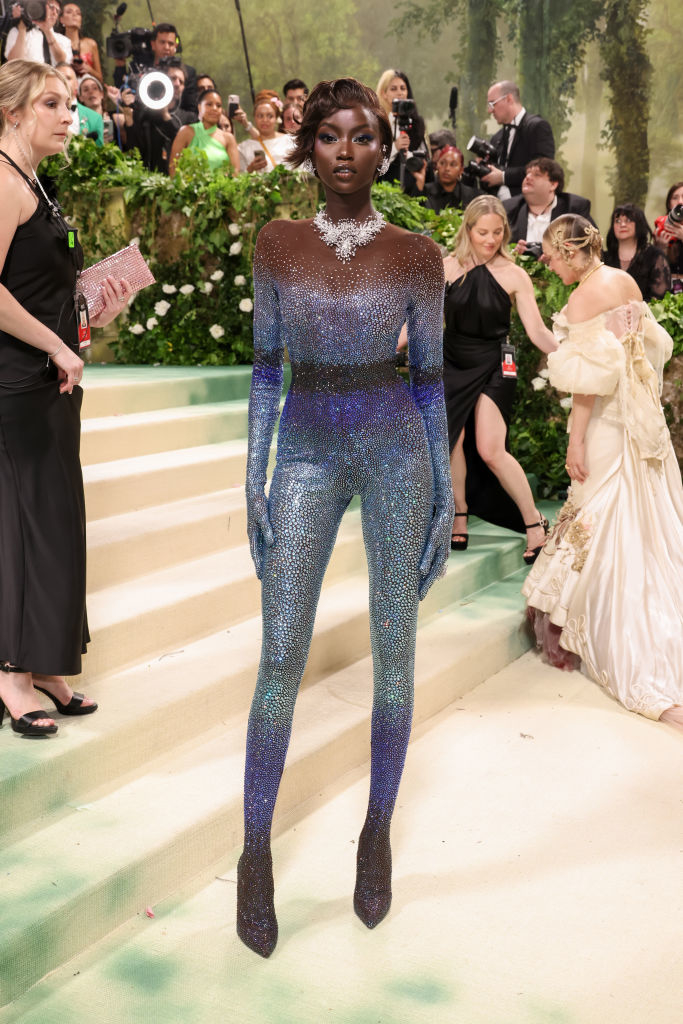 Anok posing at an event wearing a sparkling, long-sleeve jumpsuit with a fitted silhouette