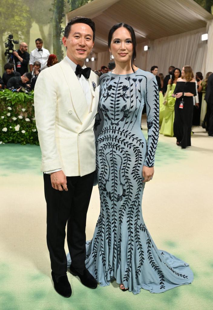 Shou and Vivian posing, one in a white tuxedo and the other in a fitted patterned gown with a flared hem