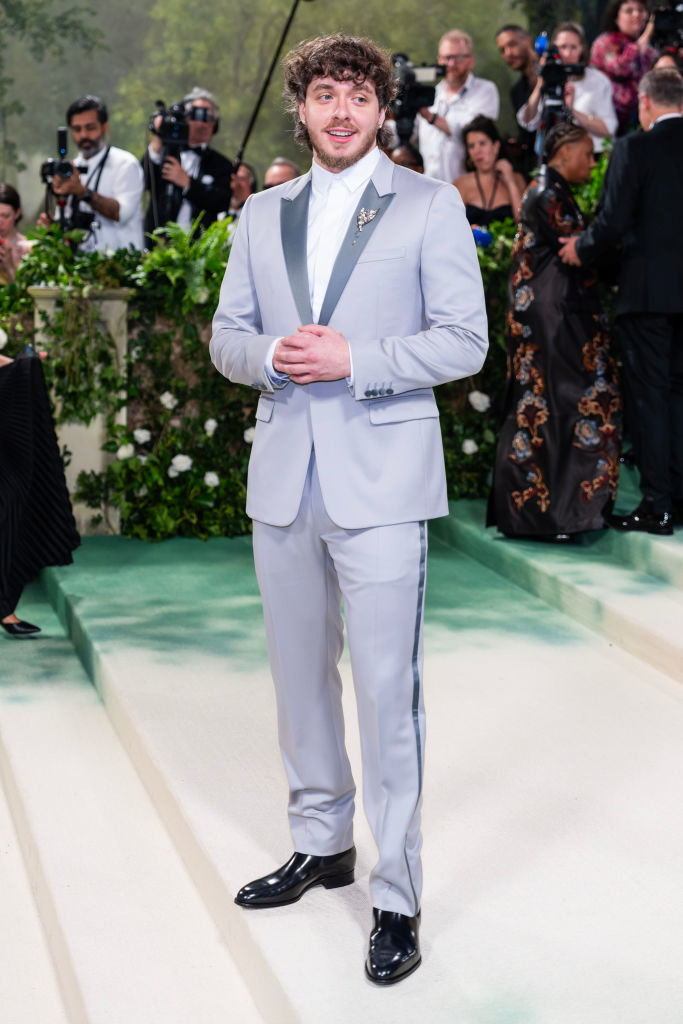 Jack in tailored light suit with dark lapels, standing on event carpet, photographers in background