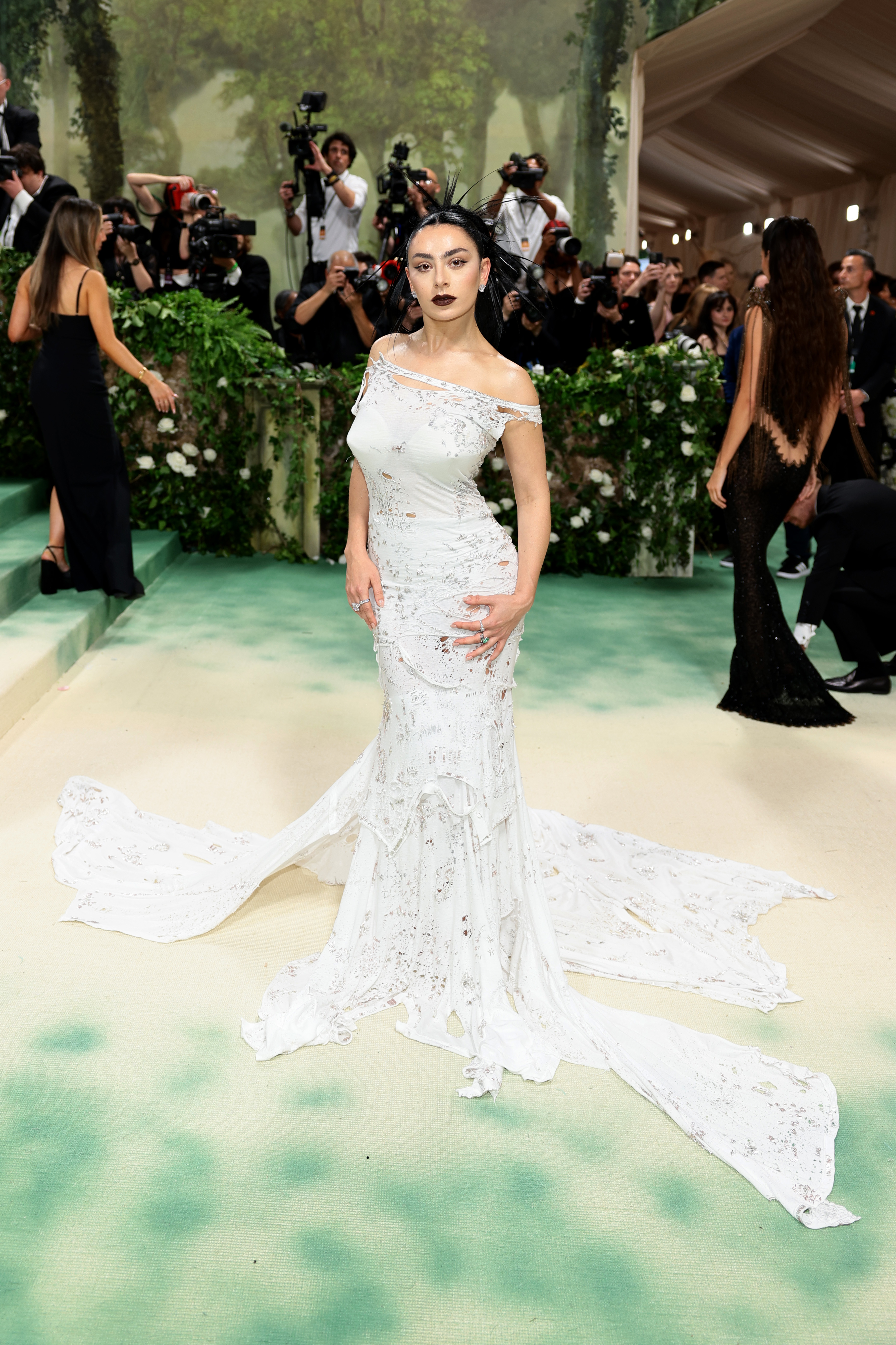 Charli XCX in an embellished white gown with a long train posing at the 2024 Met Gala