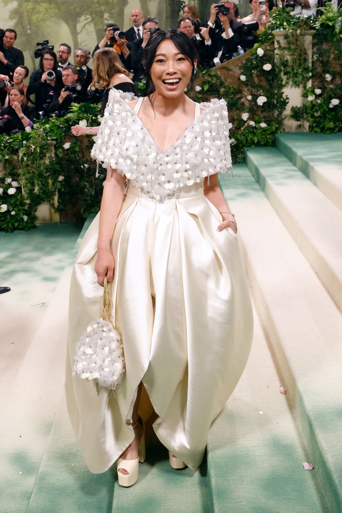 Awkwafina in an off-the-shoulder, embellished gown with a clutch, posing on event stairs
