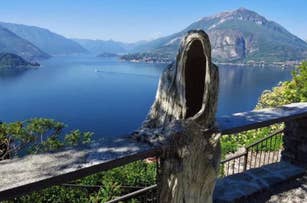 Sculpted open-mouthed figure overlooks a scenic lake with mountains in the background