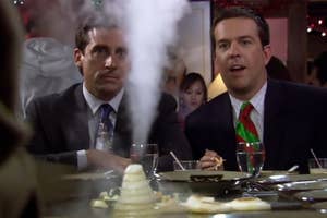 Michael Scott and Andy Bernard sitting at a table with a smoking pile of food between them in a comedic scene
