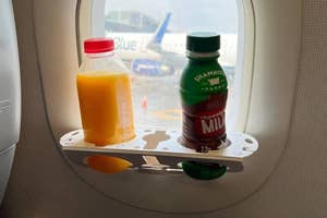 Two bottles, one of orange juice and one of milk, on an airplane window organization unit