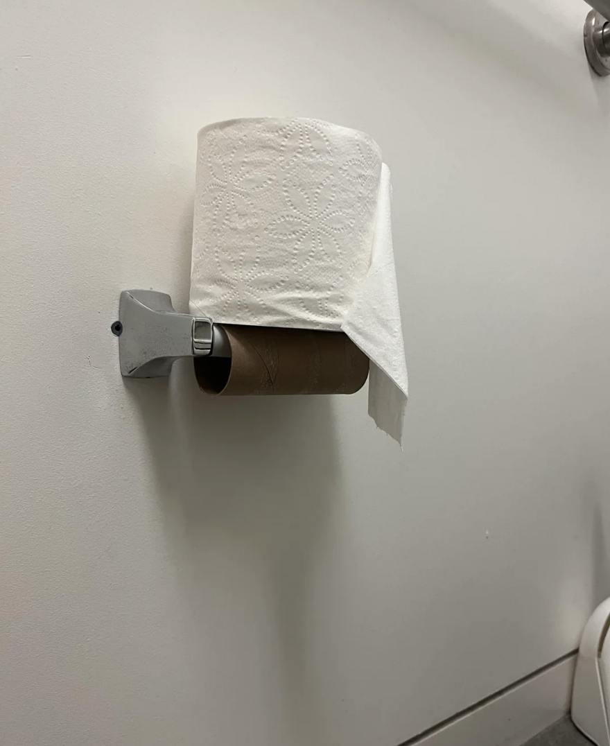 Roll of toilet paper almost finished, mounted on a dispenser, with one sheet hanging down