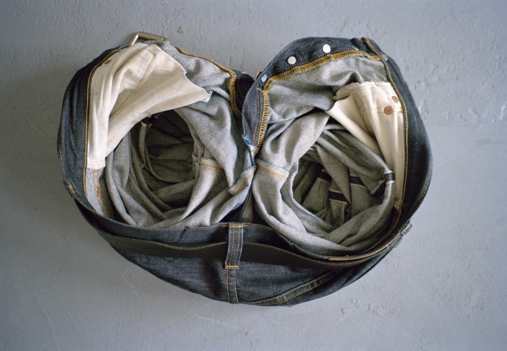 Denim jeans twisted to form an infinity symbol on a plain background