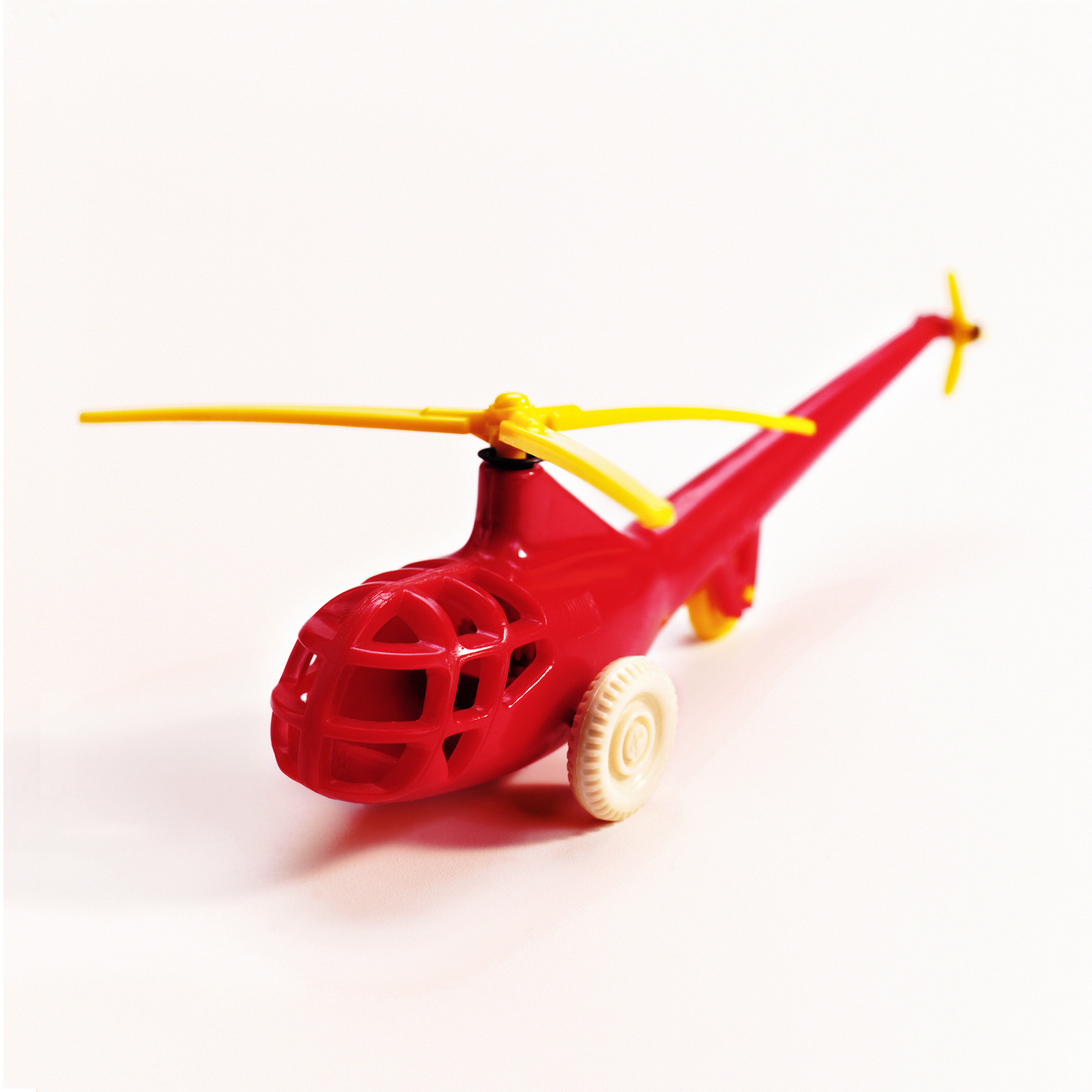 Red toy helicopter with spinning rotor blades and wheels against a white background