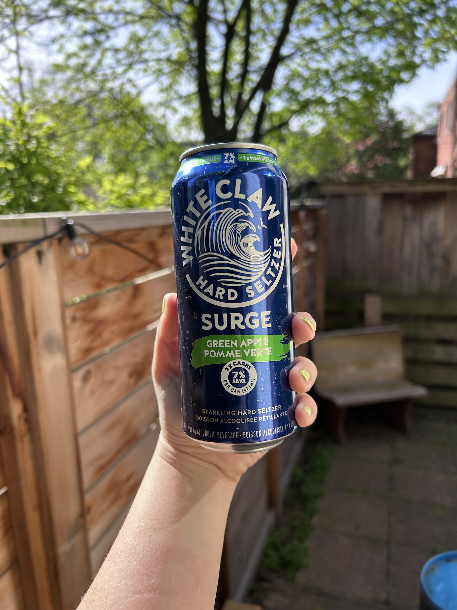 Hand holding a can of White Claw Hard Seltzer with a green apple flavor, outdoors