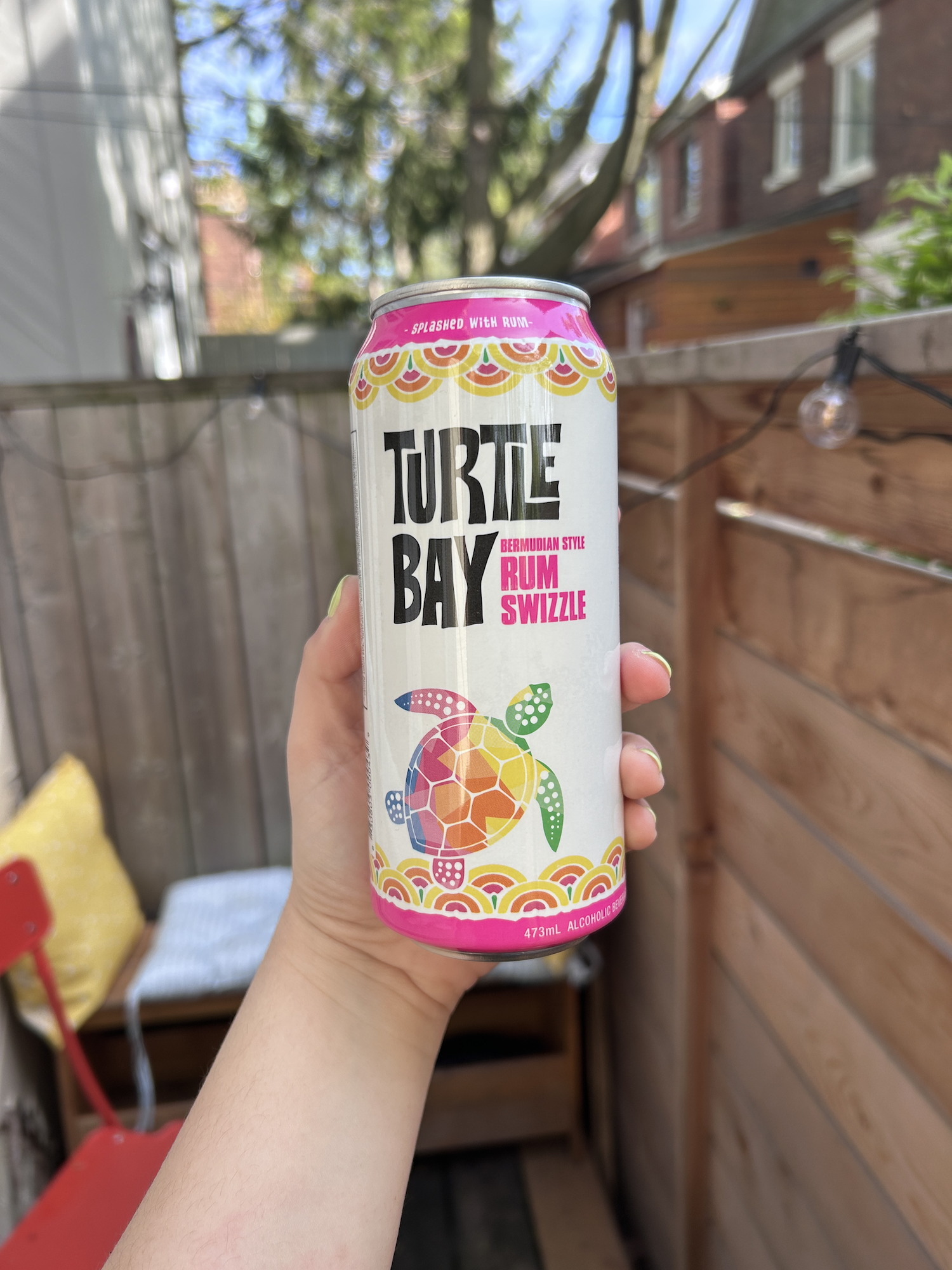 Hand holding a can of Turtle Bay Caribbean style Rum Swizzle against a backyard setting