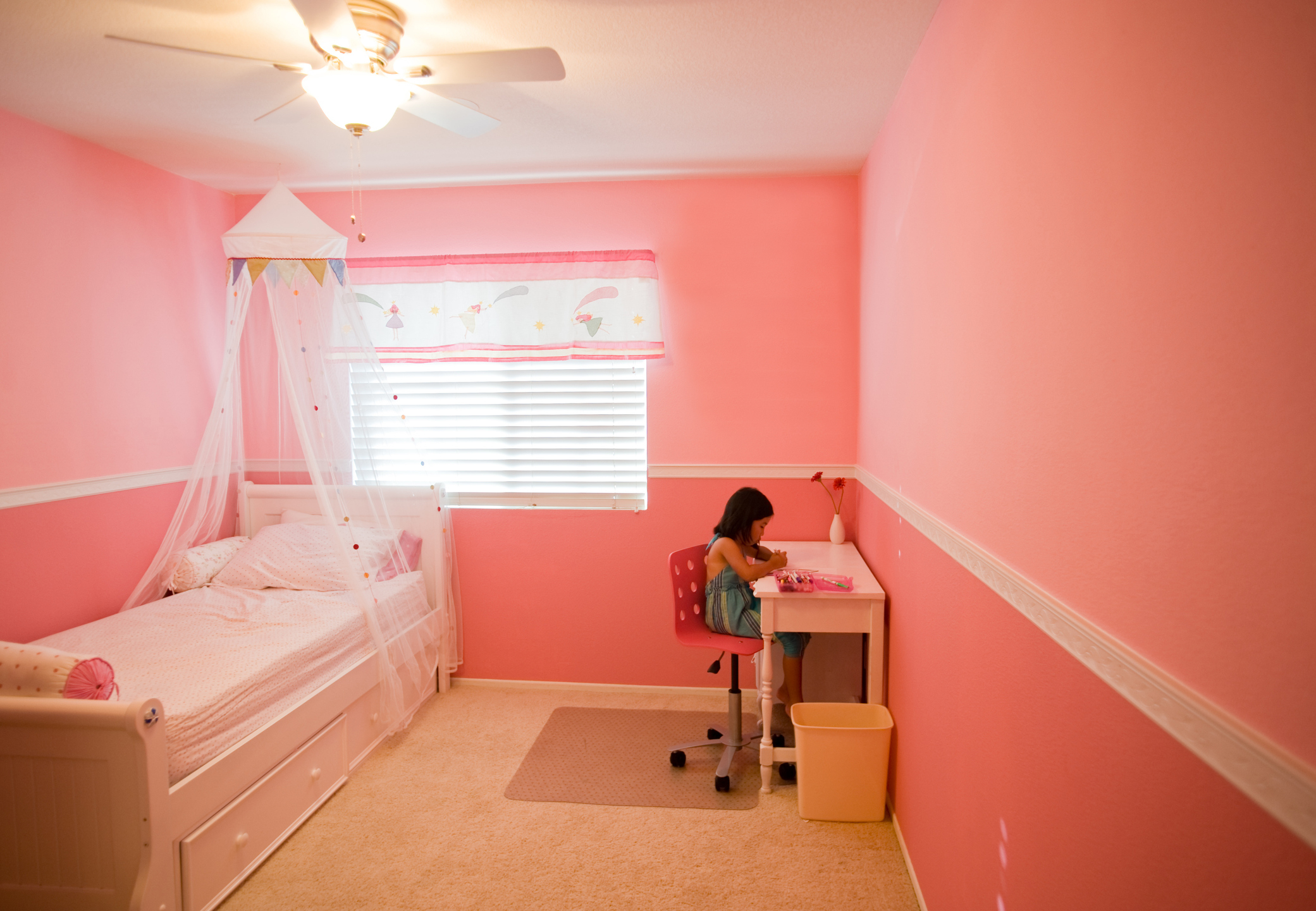 Child focusing on an activity at a desk in a pink-themed bedroom