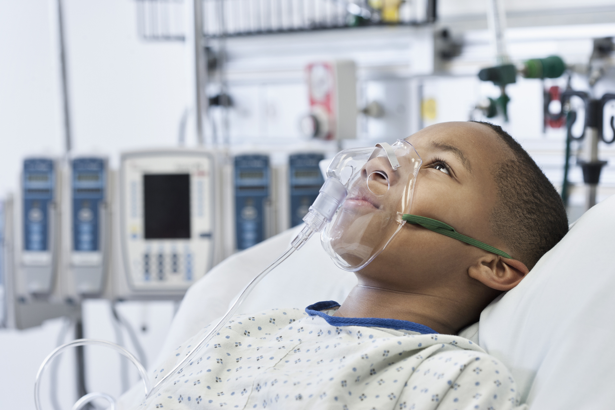 Young boy in hospital bed wearing an oxygen mask with medical equipment in the background