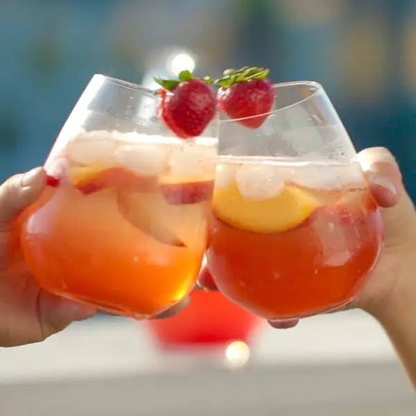 Two hands holding glasses of sparkling fruit punch toast, with strawberries garnishing the drinks