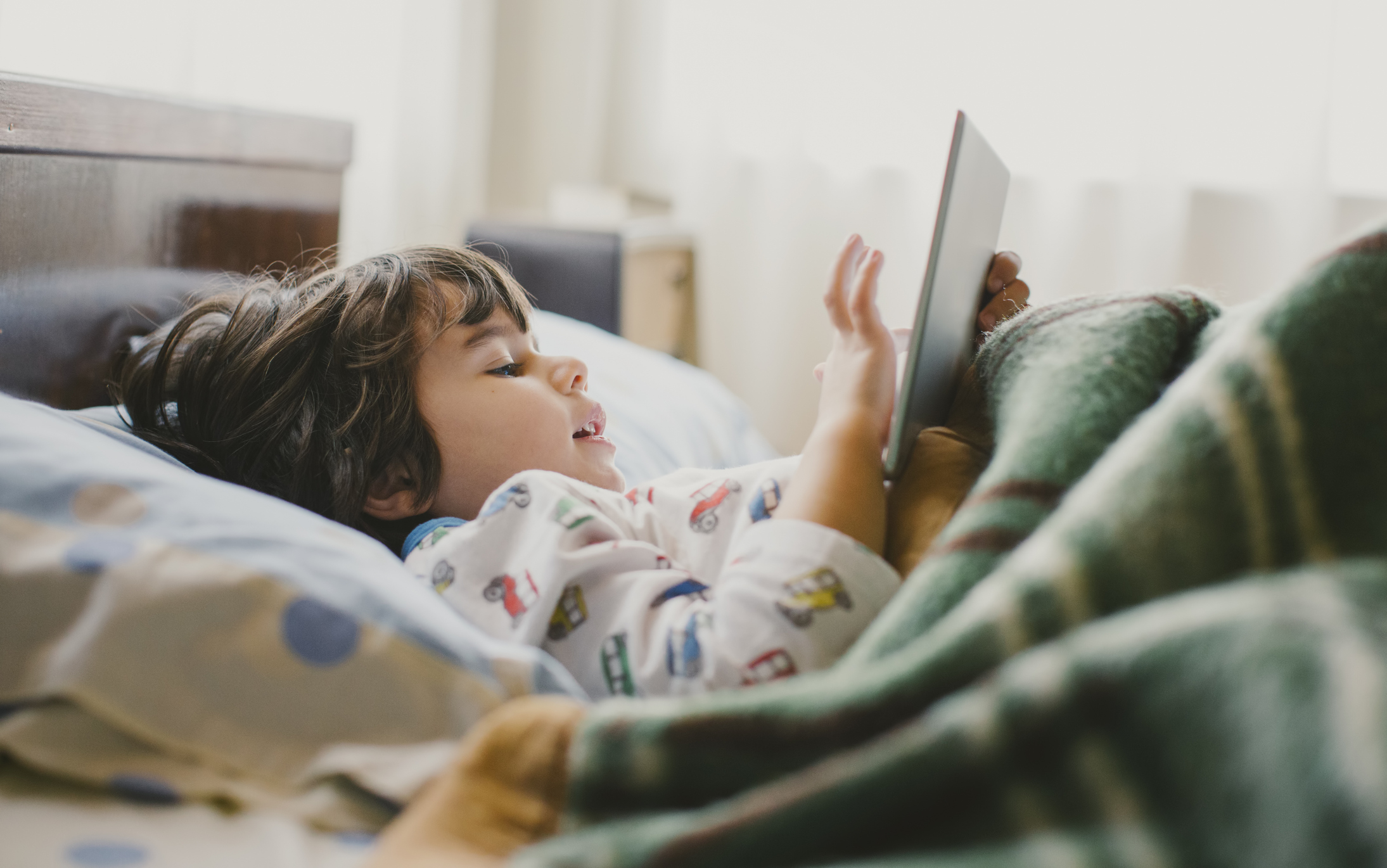 Child lying in bed holding a tablet with a joyful expression