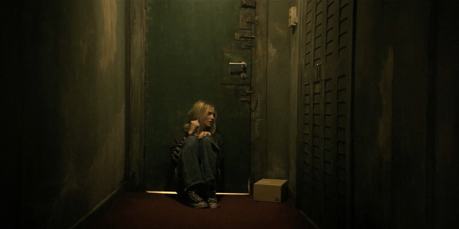 Sasha Luss in a dimly lit corridor, looking towards a door, expressing concern in Latency