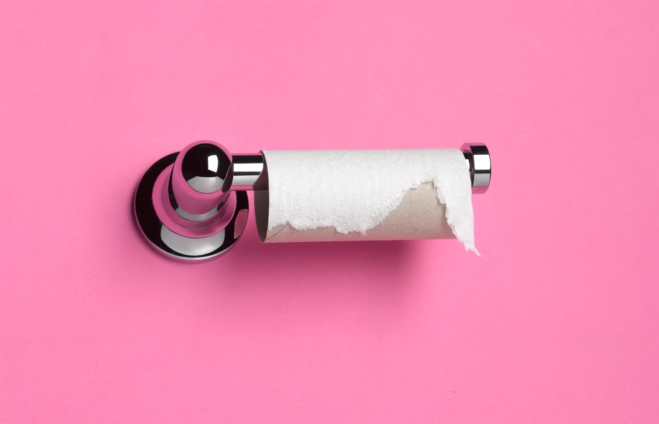 Toilet paper roll nearly empty on a metal holder, against a pink background