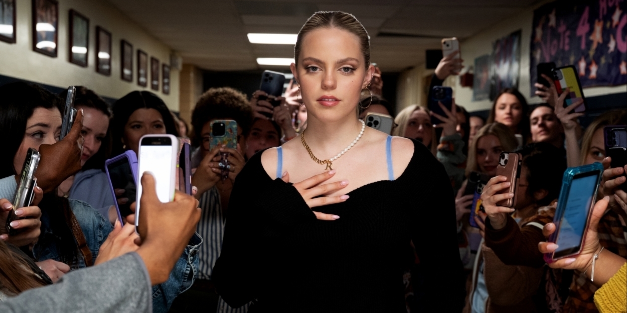 Woman in a black top walking through a crowd, people around her are taking photos with their phones