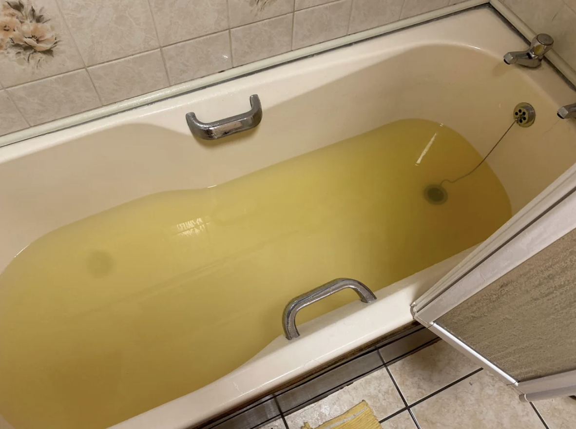 A bathtub filled with yellow water, featuring safety grab bars on the side and back wall