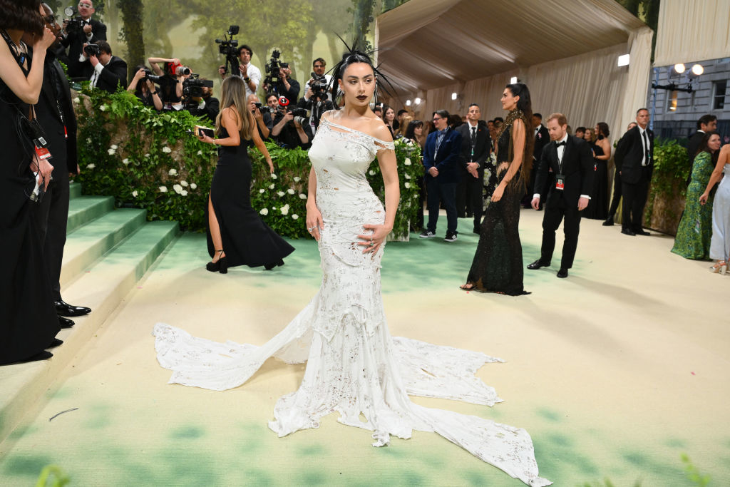 Person on a red carpet in a detailed white gown with a long trail, photograpers in background
