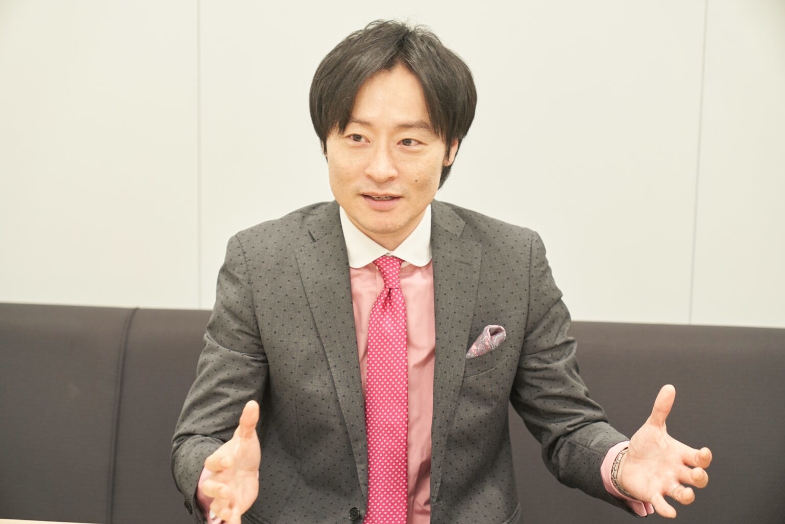 スーツとピンクのネクタイを着用した男性が話している様子。