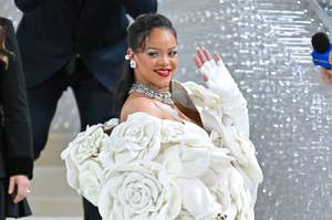 Rihanna in a voluminous white flower-themed gown with a matching long gloves waves at an event
