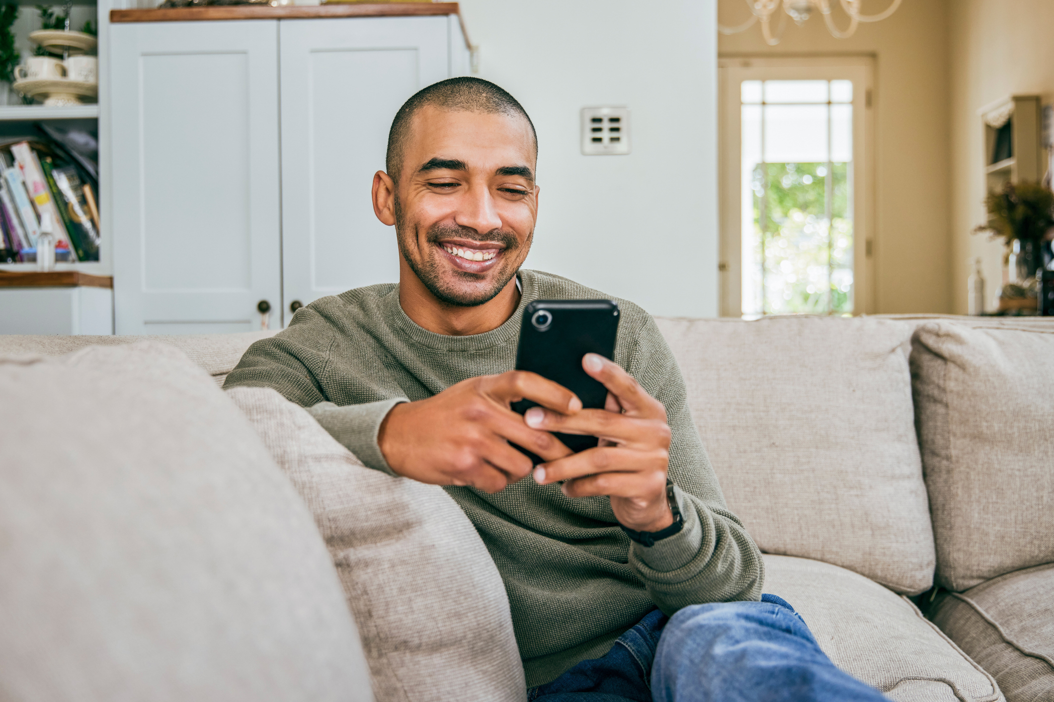 Man on couch smiling at his smartphone, possibly managing finances or remote working
