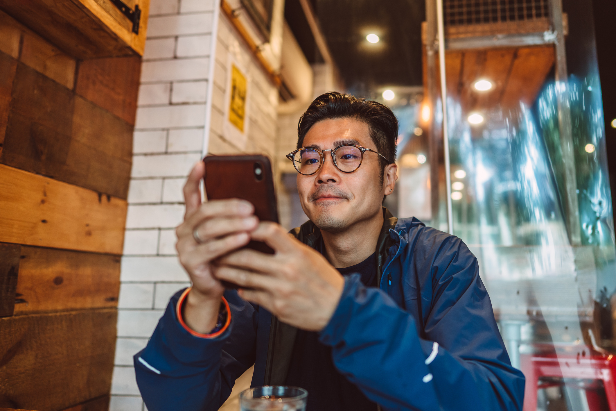 Man in glasses using smartphone at cafe table, possibly managing work or finances